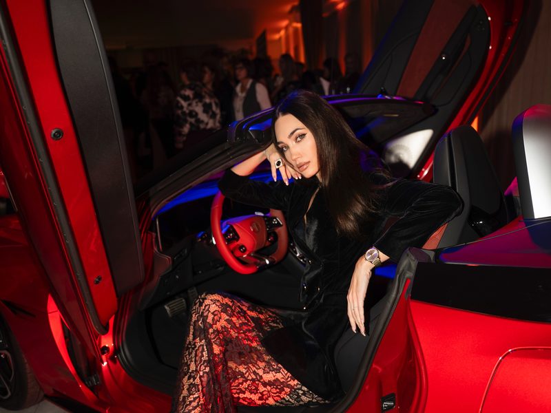 Dubravka Švegar u crnoj kombinaciji s čipkastim hlačama, za upravljačem crvenog automobila