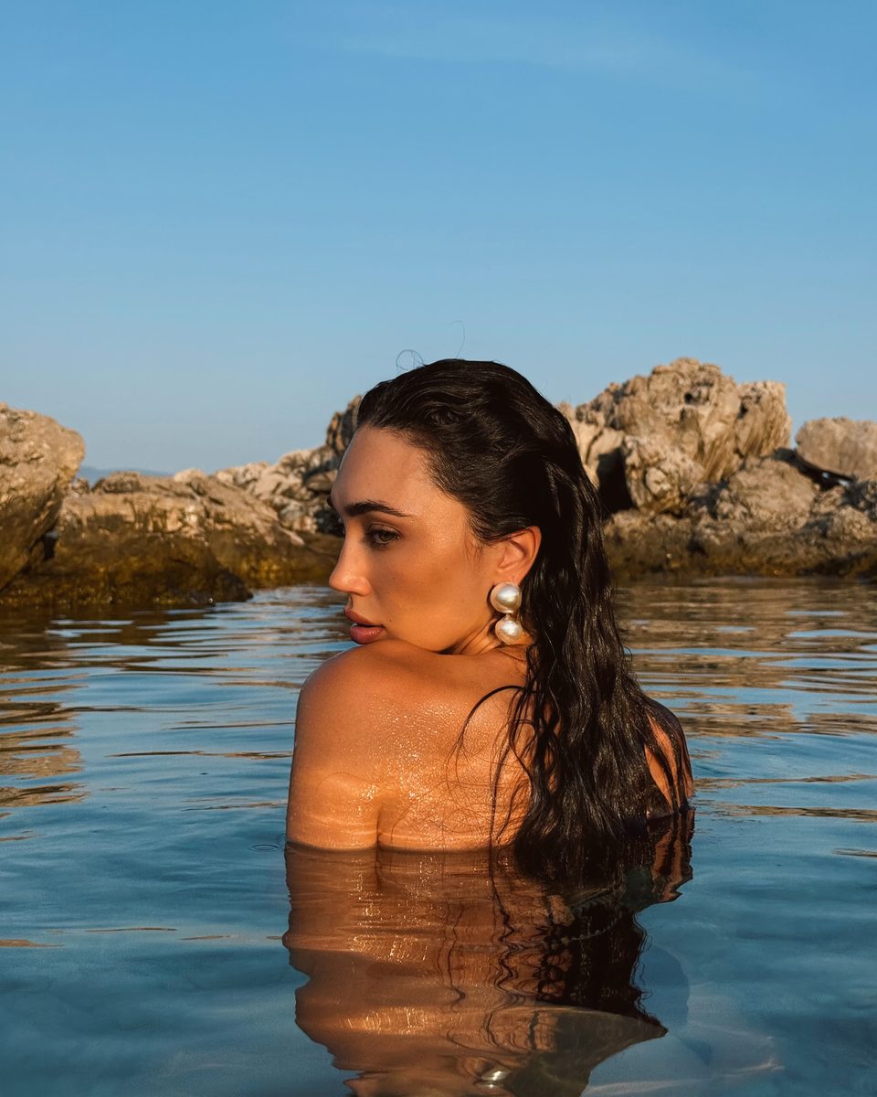 Dubravka Švegar in the sea up to her shoulders, with wet hair and pearl earrings, by the rocks